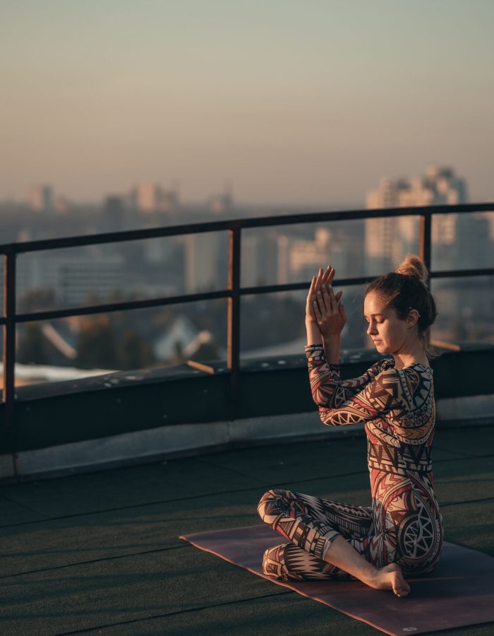 Woman doing yoga on the roof of a skyscraper in big city. Sunset