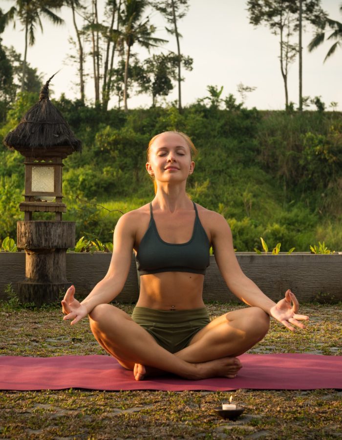 Young woman meditating in lotus posture at sunset with candles